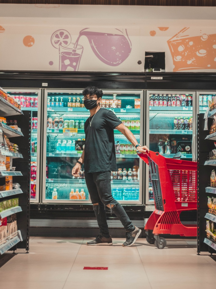 A boy holding a trolley near the fridge in a supermarket